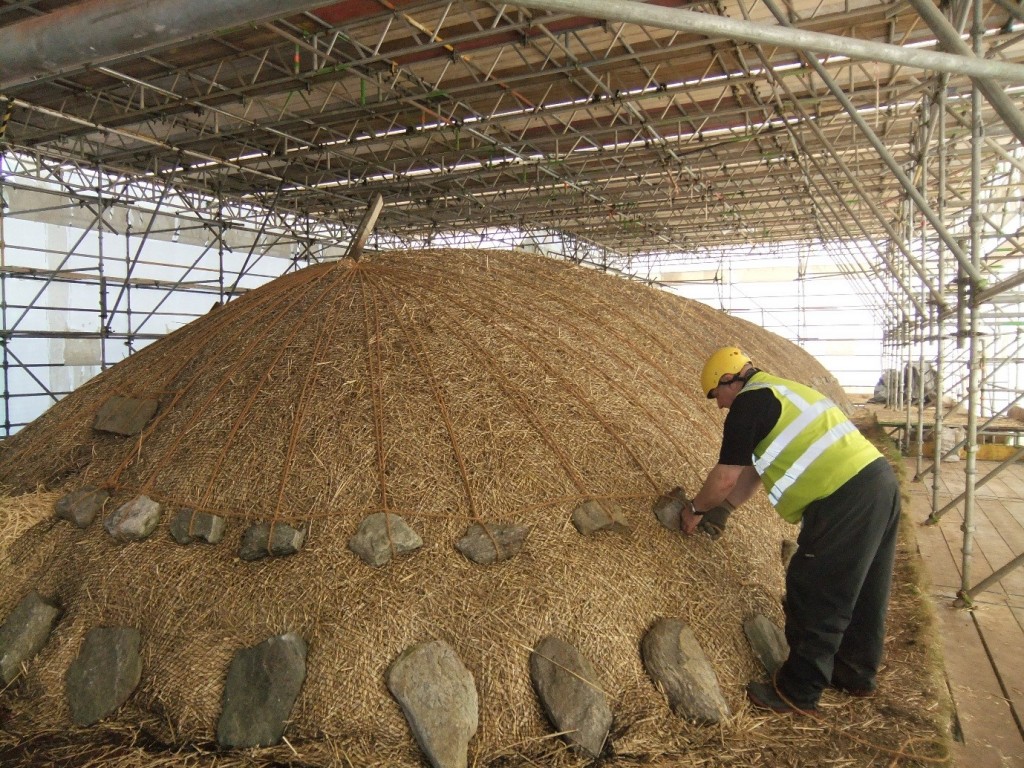 A man placing a stone on the thatched roof of Arnol blackhouse