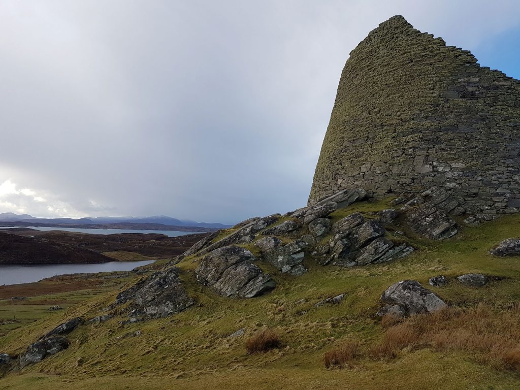 A photograph of a broch with a cloudy sky behind.