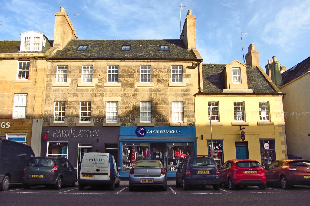 sandstone tenement building with newly painted blue Cancer Research shop front and parked cars in front
