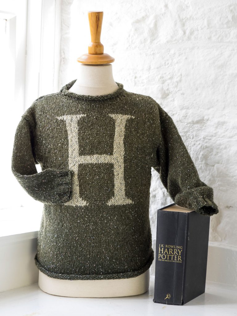 A photograph of a mannequin wearing a dark grey jumper with an H on it, beside a book entitled Harry Potter and the Order of the Phoenix