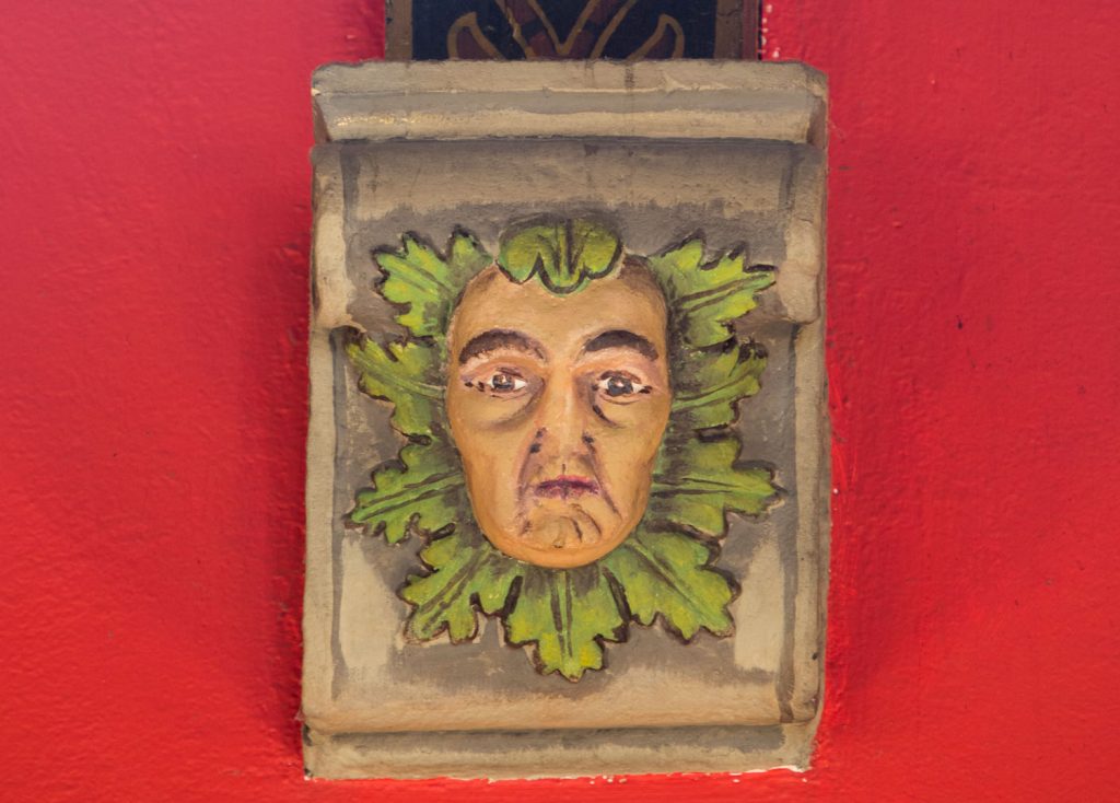 A photograph of a painted wooden carving of a man's face surrounded by leaves