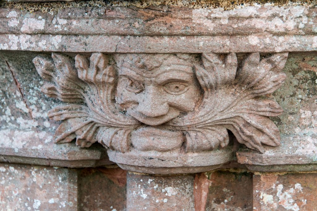 A photograph of a stone carving of a man's face eating leaves
