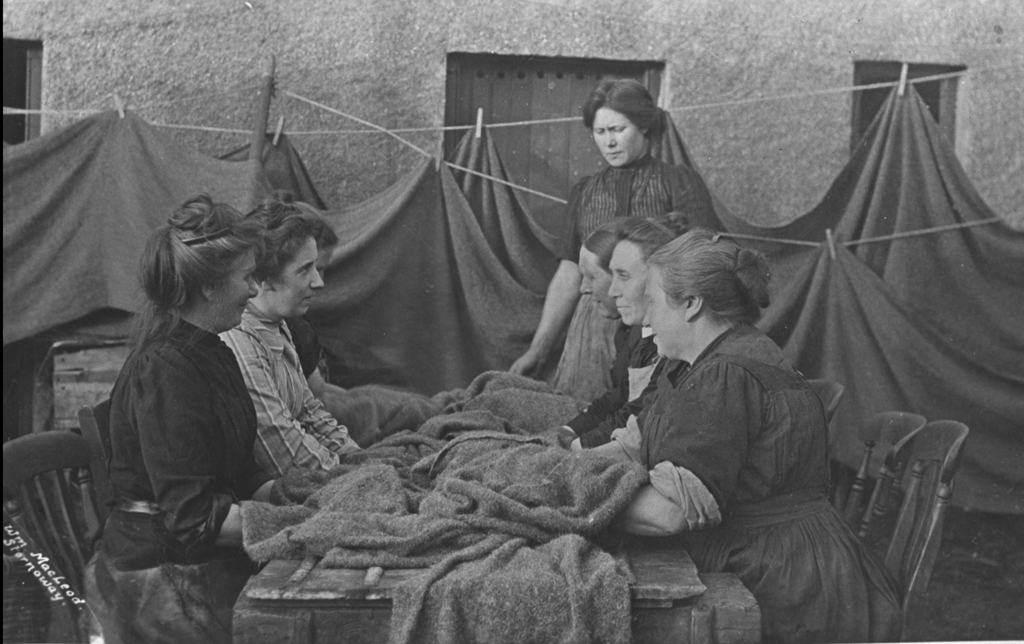 A black and white photograph of a group of women around a table with their hands on fabric.