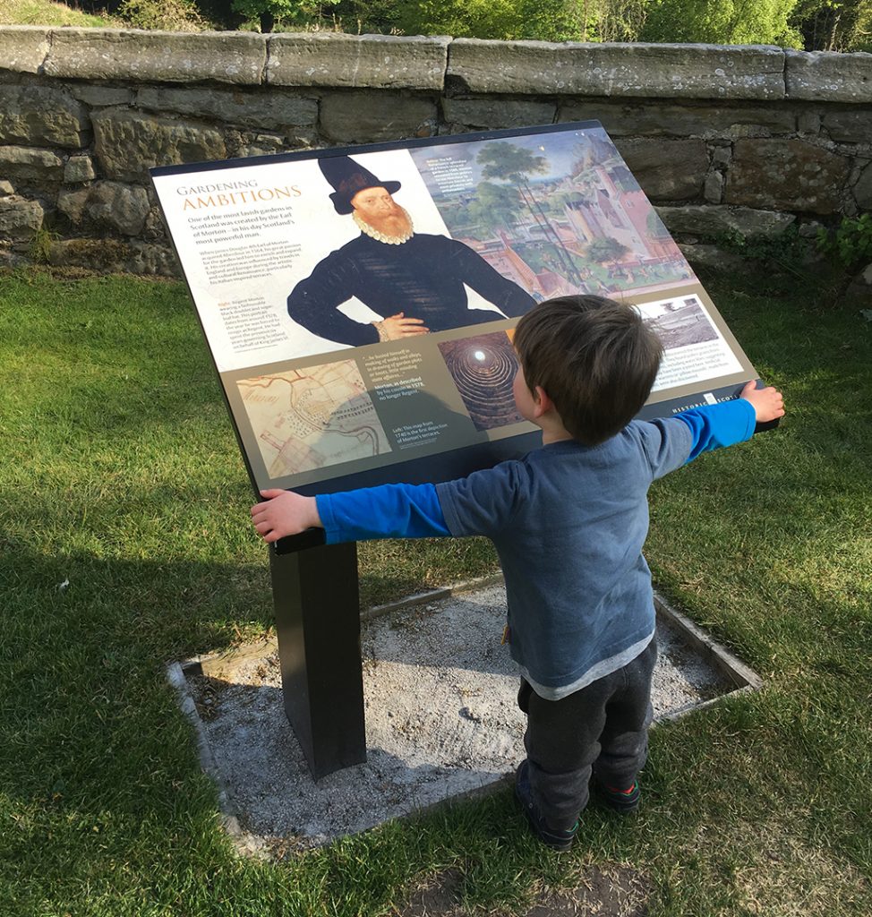 small boy with arms outstretched looks at sign with text and photo of bearded renaissance figure