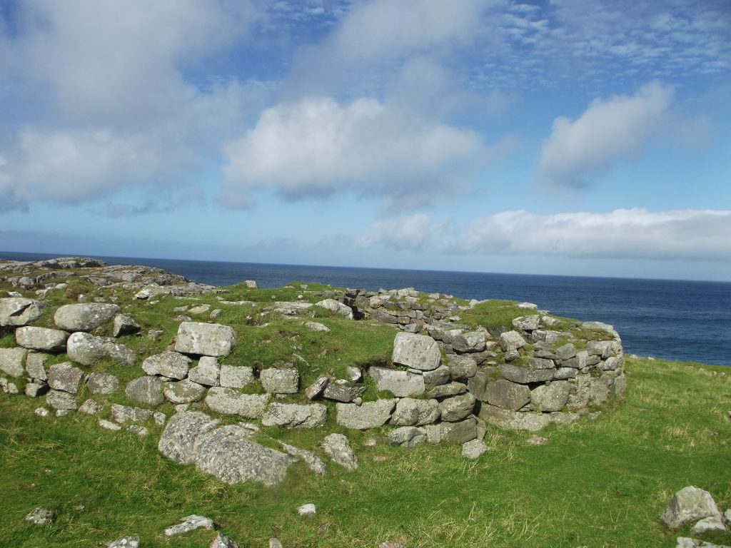 a low wall of grey bricks covered in moss and turf with the sea behind it