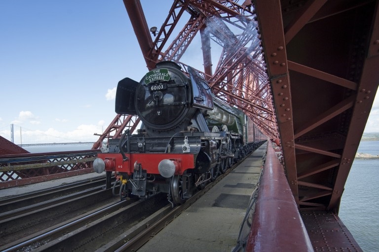 green and black steam train crossing the red painted steel Forth Bridge