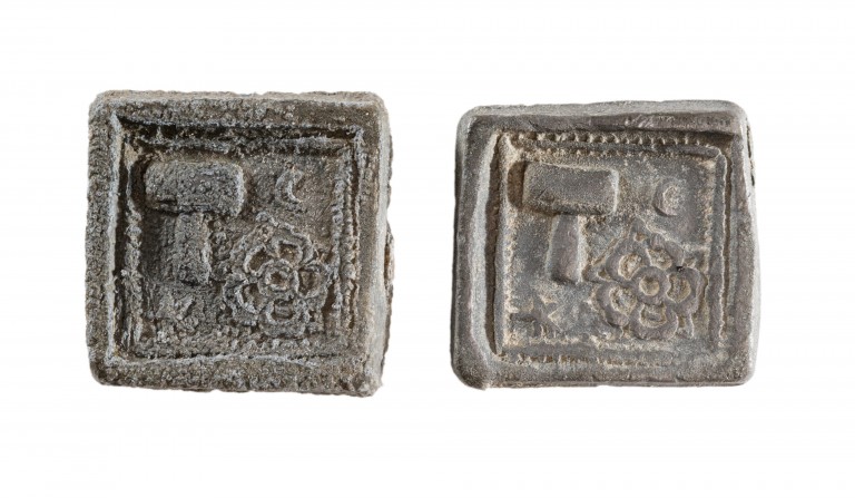A photograph of two square artefacts with carvings on the top of a hammer and a flower