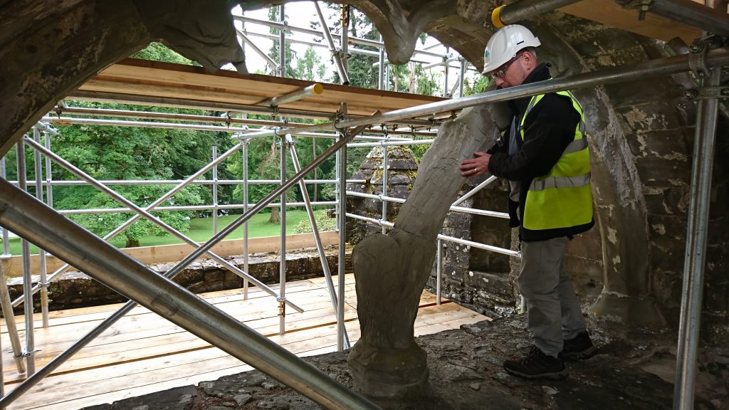 man in hi-vis vest and hard hat stands by scaffold in an old arched window examining an ancient fragment of stone