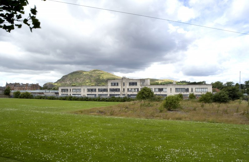 art deco building in state of direpair with mountain behind and green grass in front