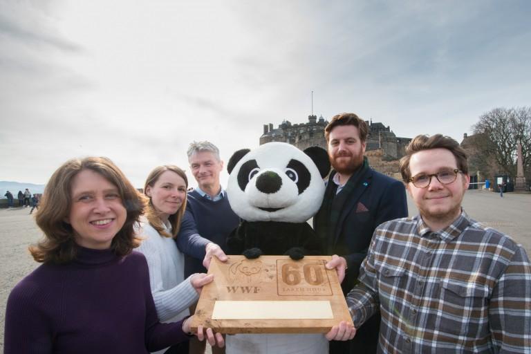 5 people and a panda stand in front of a castle holding a trophy and smiling at the camera 