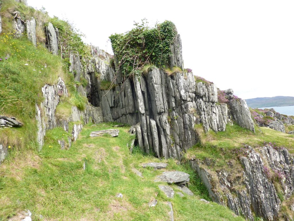 rock face on a grassy slope with a dark space showing the entrance to a cave