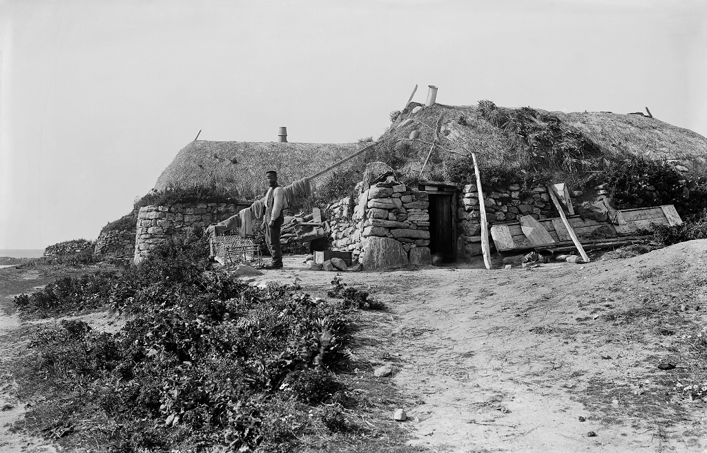 black and white photo of thatched blackhouses with man standing outside