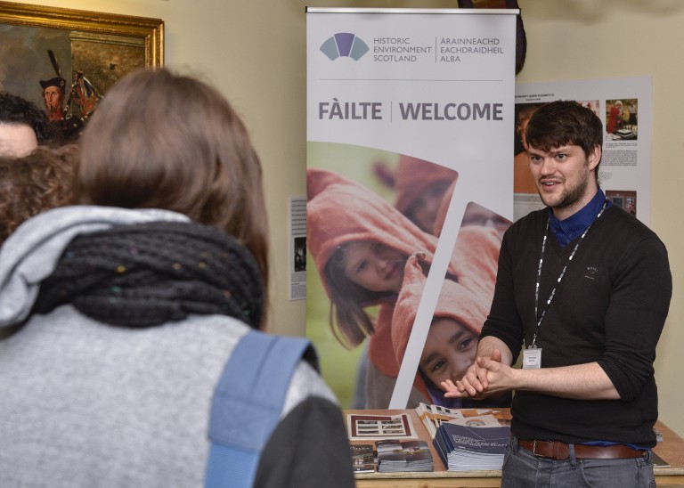 back of a person who is facing a man next to a banner with Gaelic writing on it