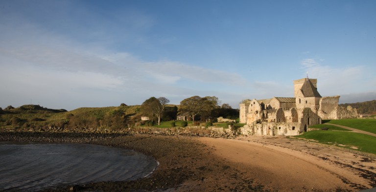 sandy bay with ruined abbey in the background beside it