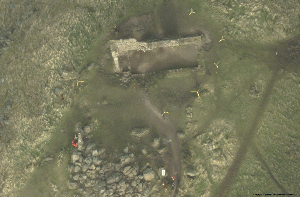 aerial view showing ruined chapel building with person in orange suit laser scanning