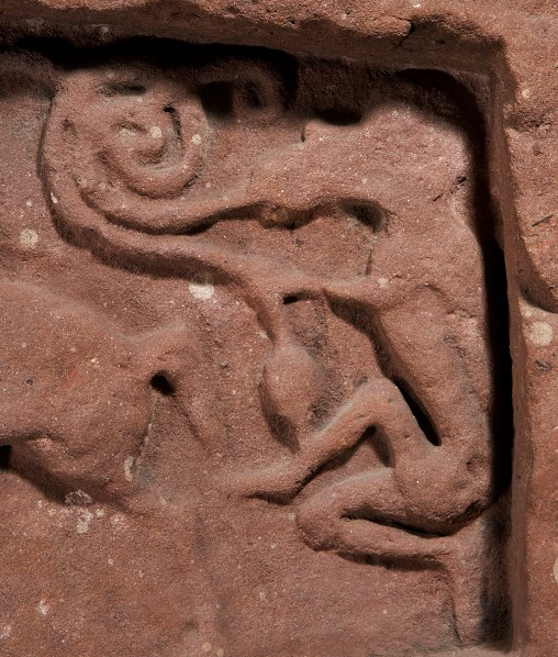 carving which shows a curious human figure with a beast's head, holding two entwined serpents in hand and mouth