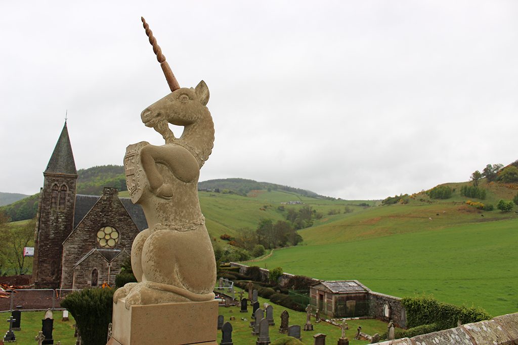 carved unicorn on a roof with church and hills in the background