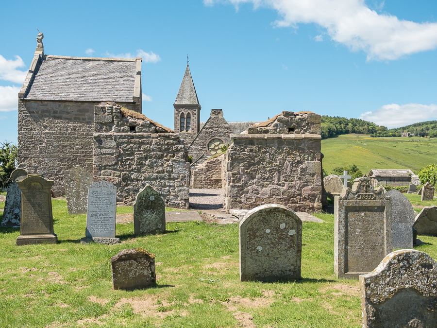 gravestones in front of a ruined church with a tower in the distance behind them