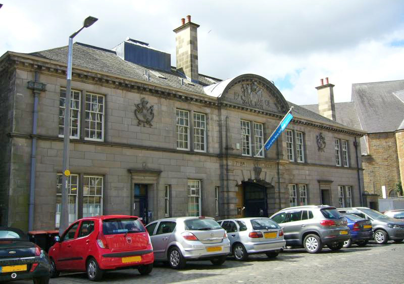 old fashioned drill hall building with cars parked outside the front and blue flag above main entrance