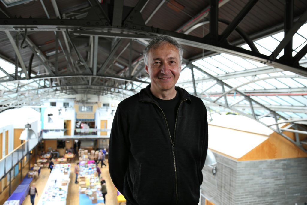 man smiles at camera from position of height with community hall visible behind him 