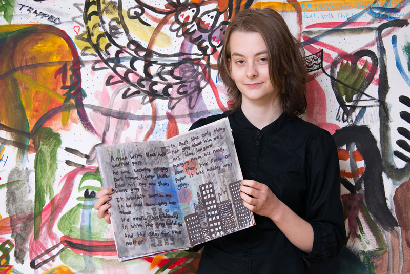 Image of a student holding up some artwork with a mural in the background