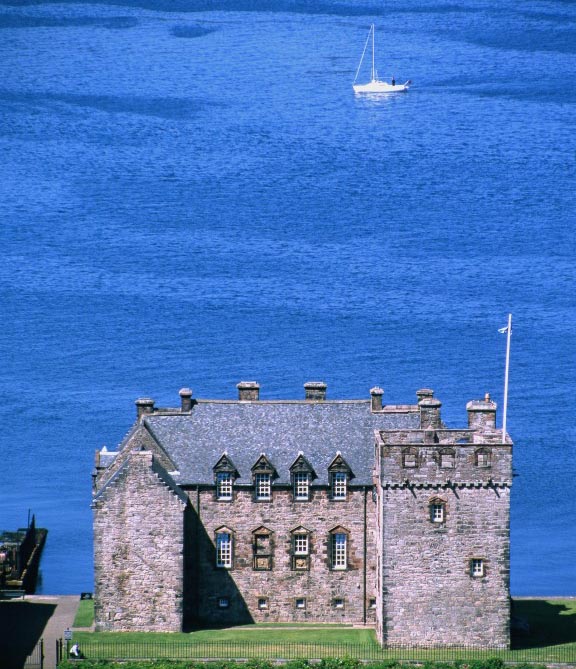 square castle building with blue sea behind and boat in the background