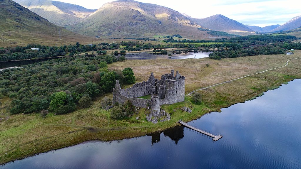 aerial image of ruined Kilchurn Castle with loch in front and mountains behind