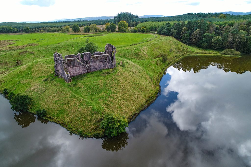 aerial view of a ruined castle on a green embankment with water in front
