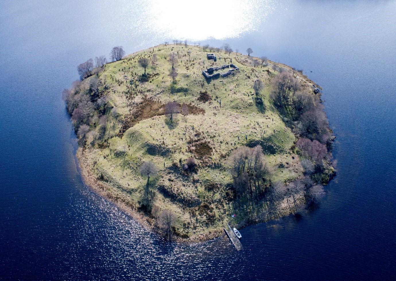 aerial view of a round island surrounded by water with a ruined building visible at one side