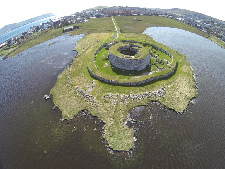 view looking down at a round stone building by the edge of some water