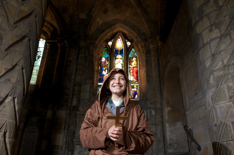 boy stands in front of stained glass window holding a cross