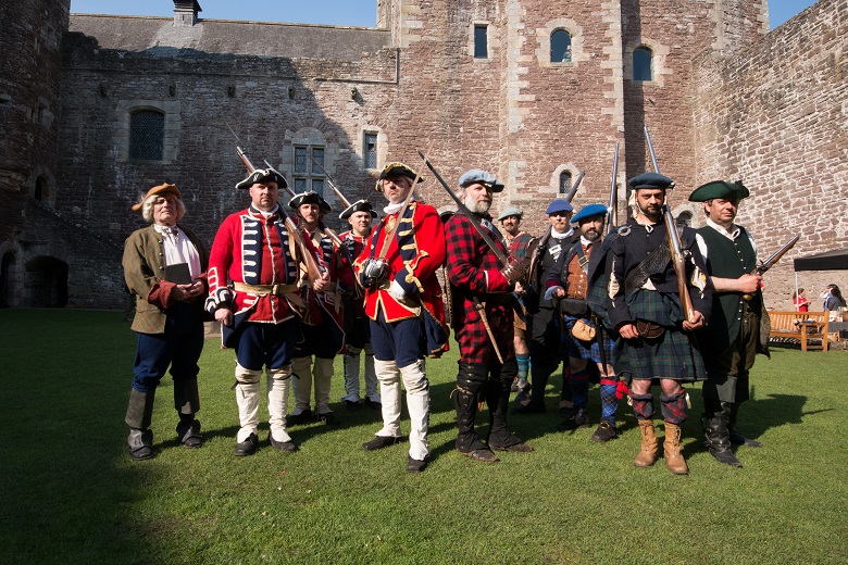 Men dressed as Red Coats and Jacobites stand in front of a castle
