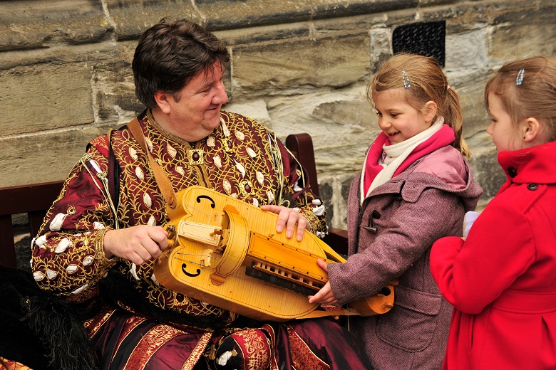 Two children meet a man in historic costume and are shown a historic musical instrument