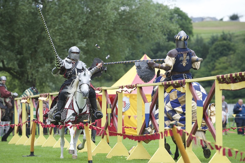 two reenactors dressed in medieval outfits charge at each other while jousting