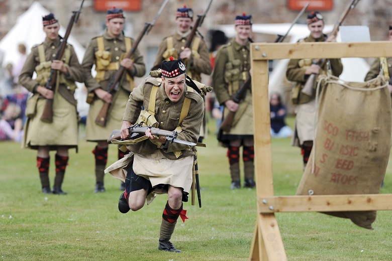 A reenactor dressed in WWI clothing charges at the camera with a rifle