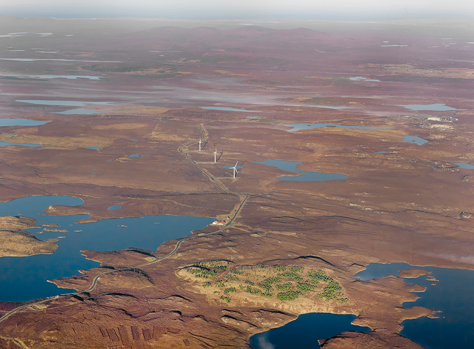 aerial image showing land bordered by water and wind turbines in the distance