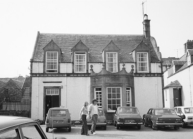 In the 1970s a couple walks in front of a pub holding hands