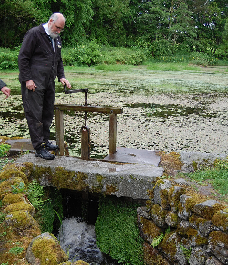 View of the mill pond at New Abbery Corn Mill with a man opening the sluice gates to let water through