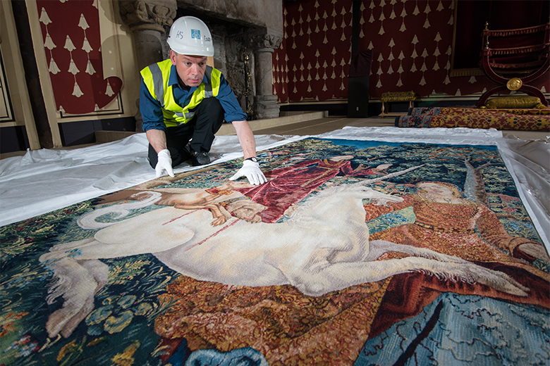 Man bends over a Unicorn tapestry on the hall floor