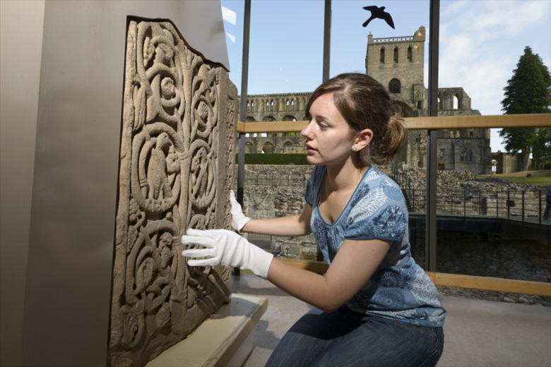 View of female conservator inspecting the carving.