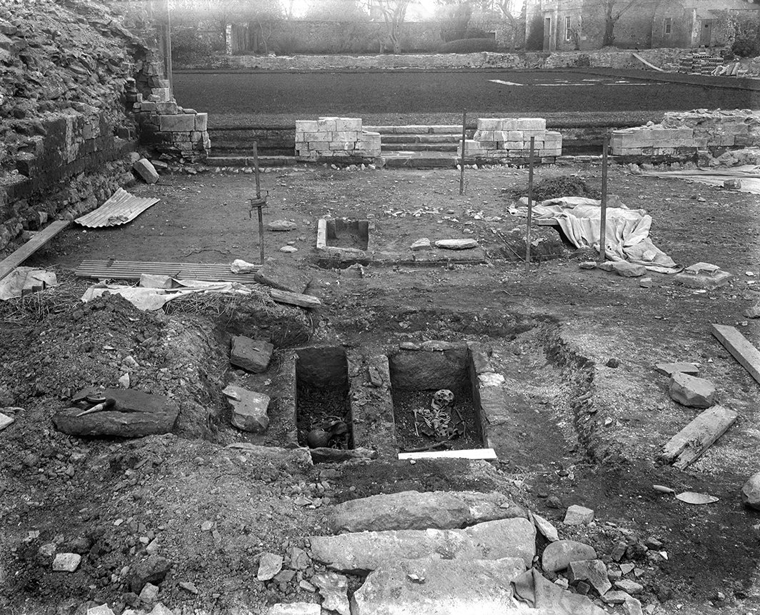 black and white photo showing excavation site with tools and holes dug in ground