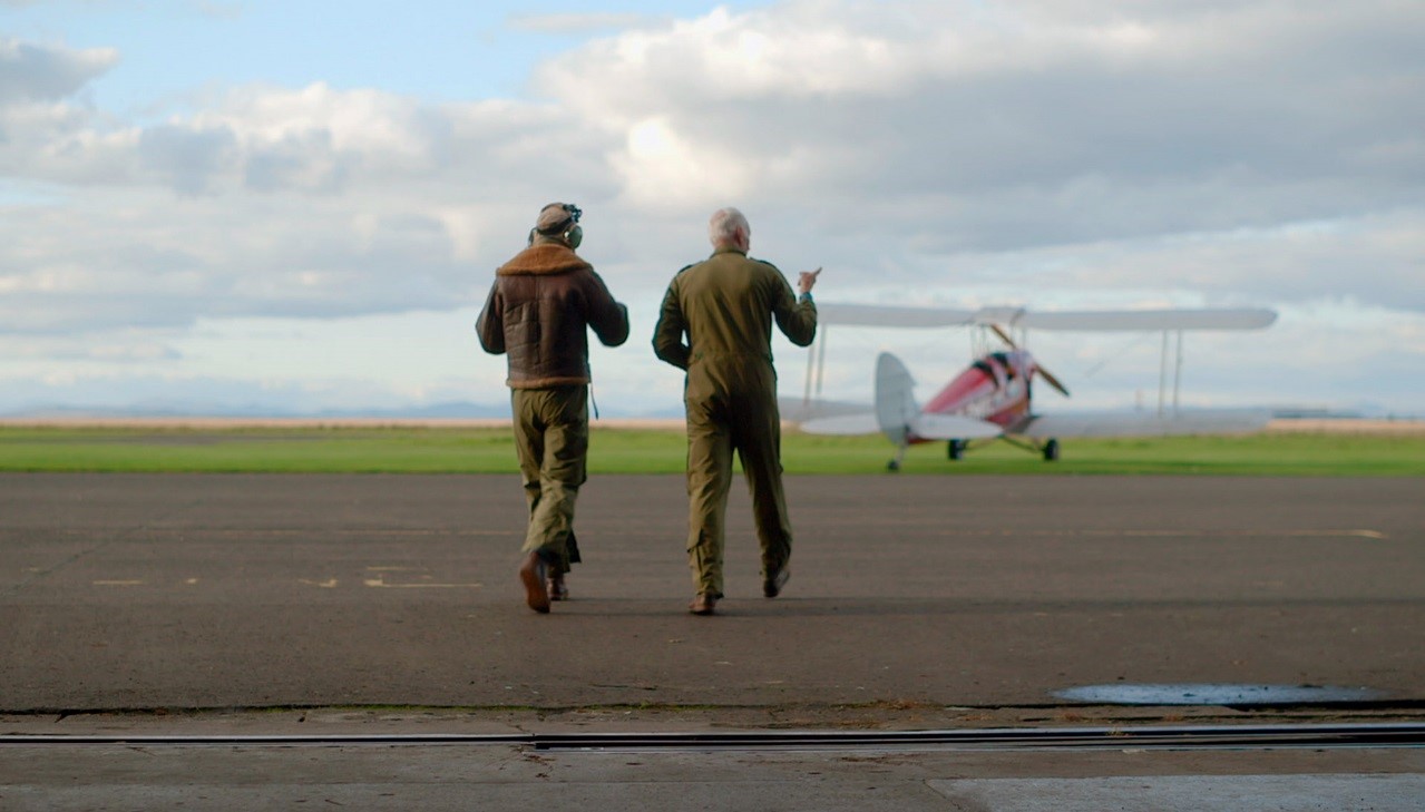 two men walk away from camera towards plane in distance
