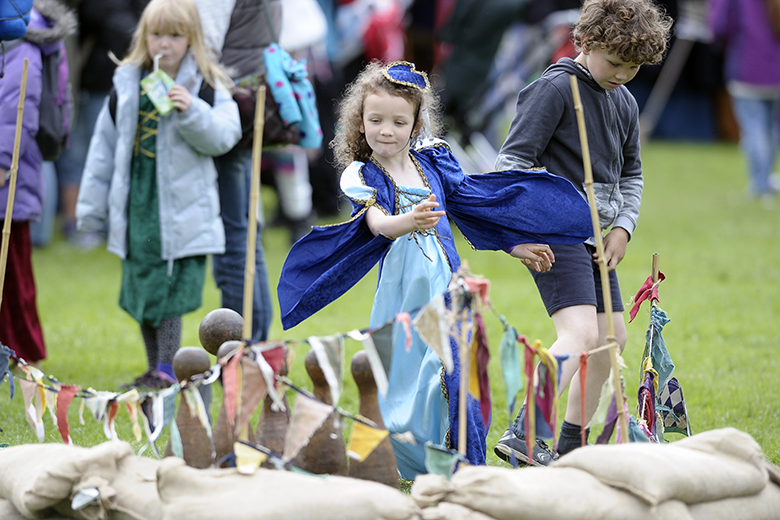 Young girl in medieval dress plays a game of skittles