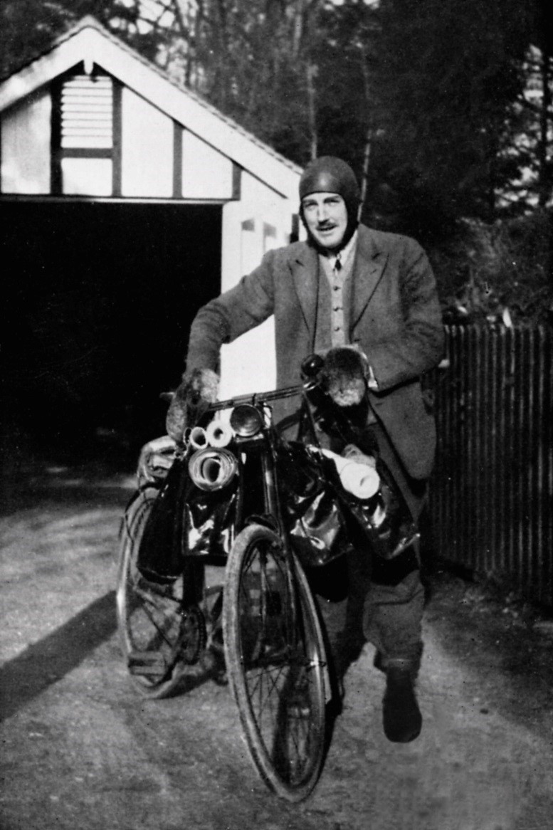 black and white photo of man next to bicyle laden with maps and survey equipment