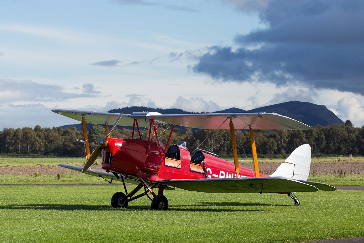 old fashioned red aeroplane with two seats and a propellor