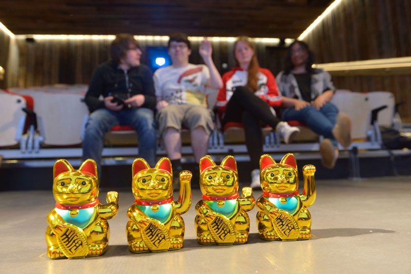 Image of a group of young artists sitting in a small cinema with a row of toy cats in front of them