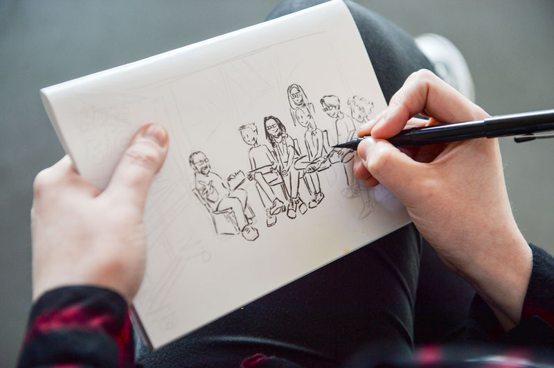 Image of a young artist sketching a group of people at a comics workshop