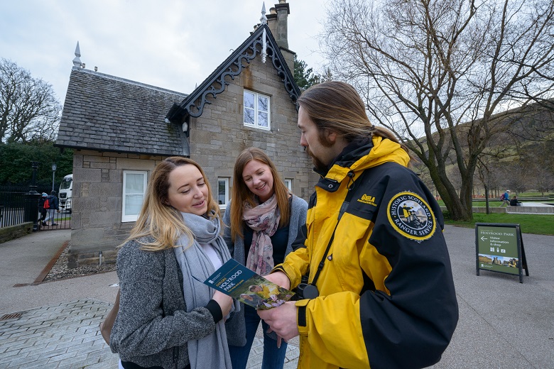 A Holyrood Ranger in a yellow coat meets visitors outside Holyrood Lodge