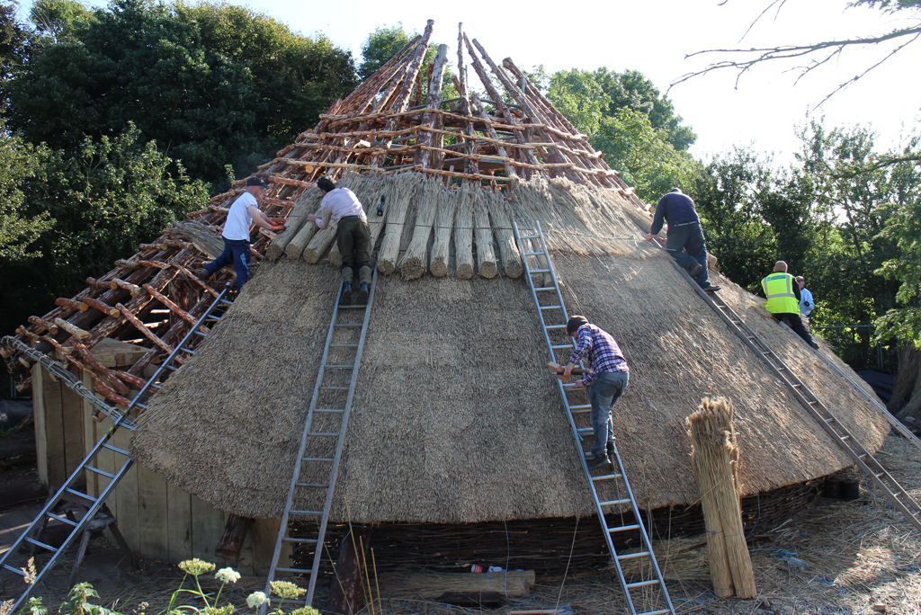 people on ladders constructing a round building with thatched roof