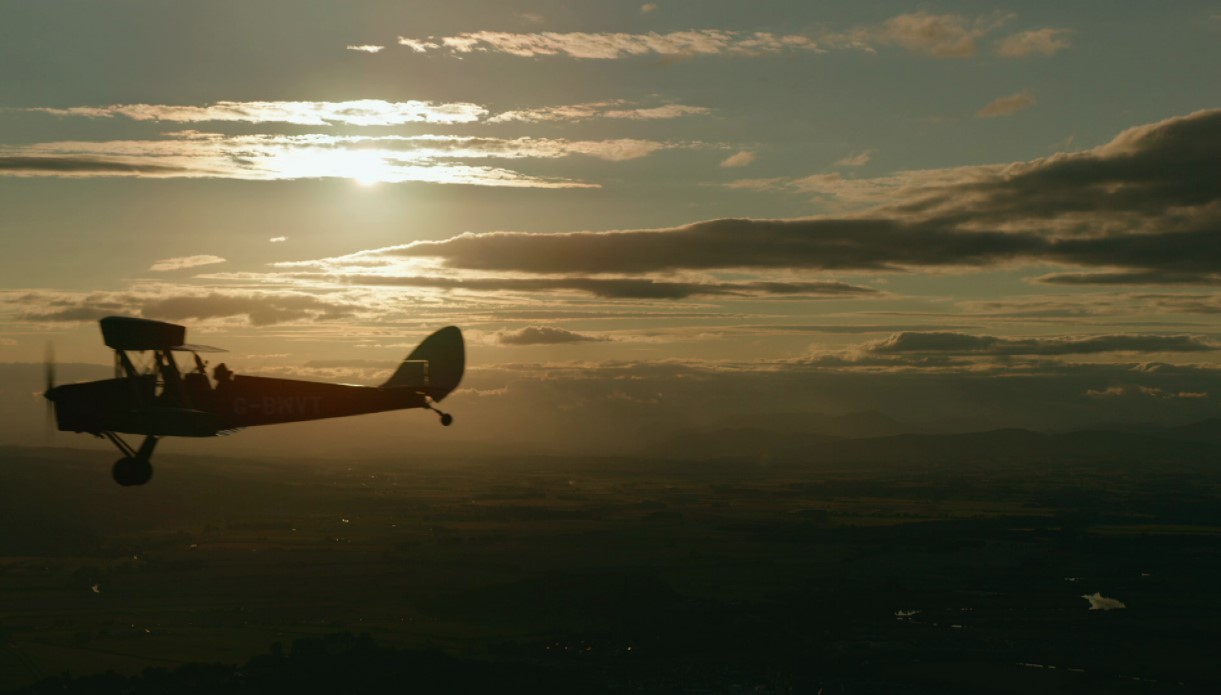 old fashioned plane in flight silhouetted against sunset